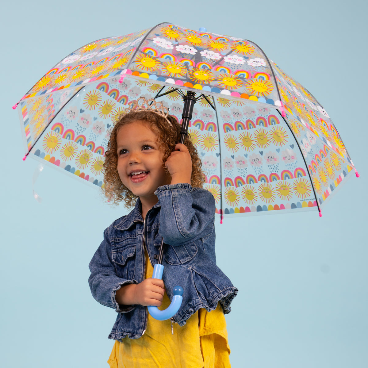 Girl using sun rainbows and clouds umbrella displaying clear dome with bright rainbow and sunshine design"