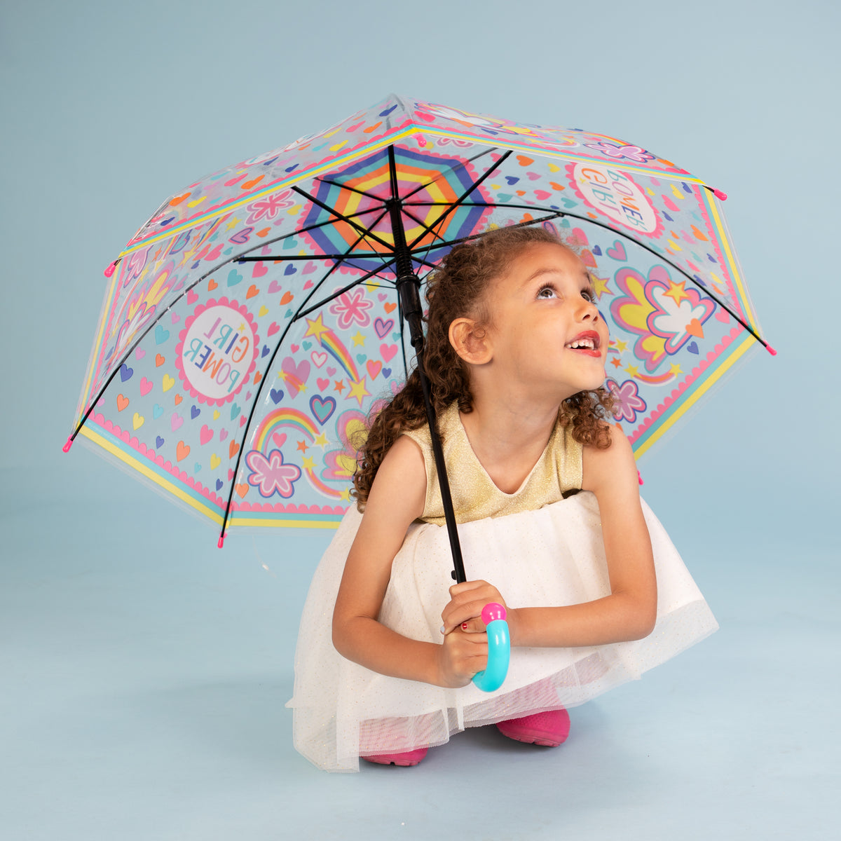 Girl holding girl power umbrella outdoors displaying clear dome with rainbow and cloud design